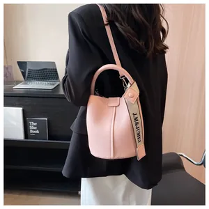 Vue détaillée d'un sac seau en cuir litchi rose avec une large bandoulière lettrée