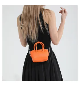 Model wearing orange pebble leather mini bag with silver chain strap on black dress