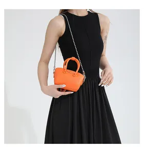 Mini orange crossbody bag with silver bead chain shown on black dress for size reference