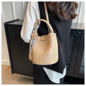 Détail du sac seau beige texture grainée avec une large bandoulière tissée logotée