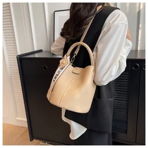 Détail du sac seau crème en cuir grainé avec bandoulière à lettres et logo