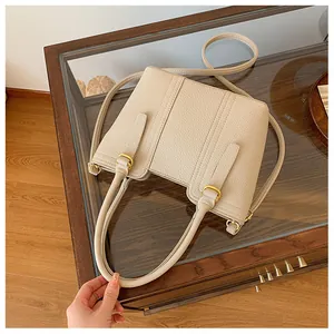 Detail view of beige lychee grain leather handbag with matte gold hardware and stitching