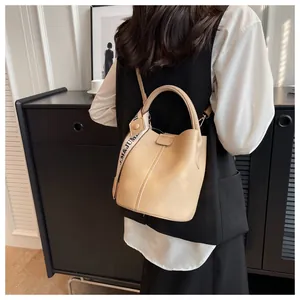 Détail d'un sac seau beige à grain litchi avec une large bandoulière décorative