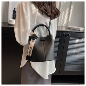 Détail du sac seau noir en cuir texturé litchi avec large bandoulière en tissu logotée