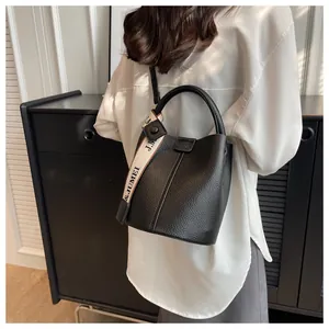 Détail du sac seau noir en cuir grainé avec large bandoulière à logo et anse