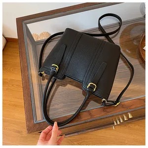 Close-up of black lychee-textured leather handbag with gold hardware on a glass table