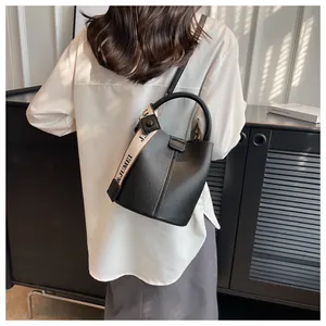 Détail du sac seau en cuir noir avec texture grainée et bandoulière tissée élégante