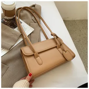Detail of minimalist beige baguette bag made of smooth faux leather with side charm