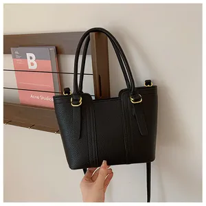 Close-up of litchi grain leather texture and gold hardware on black tote bag