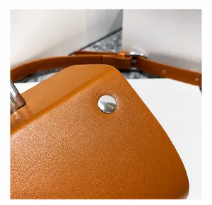 Detailed close-up of orange leather bag with polished silver rivet and precise stitching