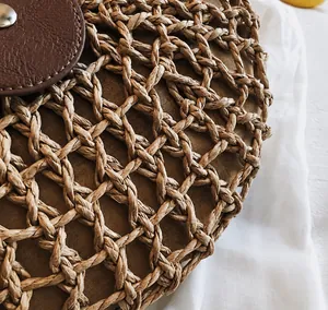 Detail der handgewebten Strohtextur und dunkelbraunen Lederklappe mit Metalldruckknopf