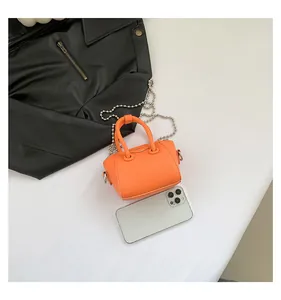 Top view of bright orange mini crossbody bag with silver chain next to a smartphone