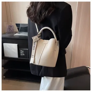 Sac seau beige en cuir grainé avec bandoulière jacquard porté à l'épaule au bureau
