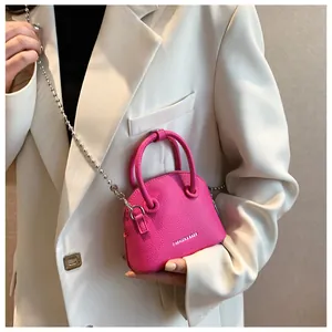 Detail of rose red mini shell crossbody bag with silver beaded chain on beige outfit