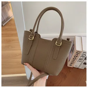 Brown lychee leather trapezoid handbag with gold rings and long strap in hand