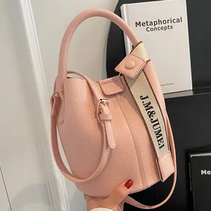 Sac seau rose en cuir grainé avec bandoulière large logotypée et poignée supérieure