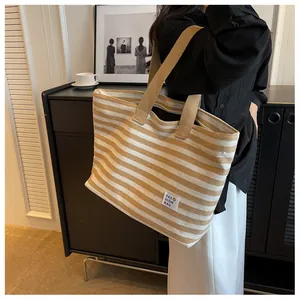 Detail of a khaki striped canvas tote bag with a fashion smiley patch worn by a model