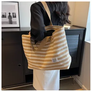 Detail of yellow and white striped canvas tote bag with fashion label and wide shoulder strap