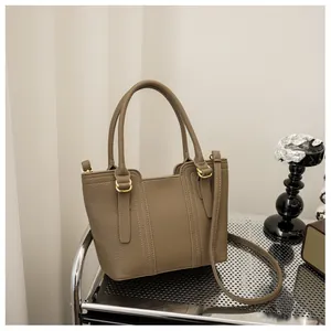 Detail view of khaki pebbled leather tote bag with gold hardware on a minimalist shelf