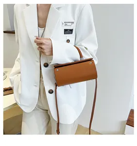 Brown cylinder crossbody bag with silver rivets styled on a white oversized blazer