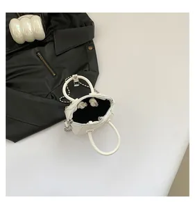 Top view of white mini trapezoid bag with silver chain strap on black leather contrast