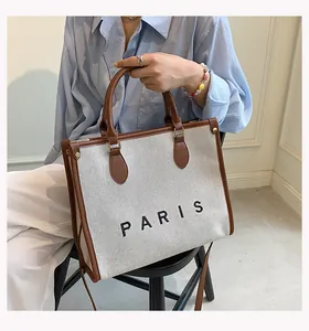 Detalle del bolso tote de lona con ribete de cuero marrón y letras PARIS en el modelo