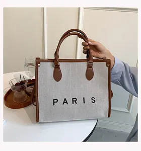 Detalle del bolso tote de lona con asas de cuero marrón y el logotipo PARIS en negro