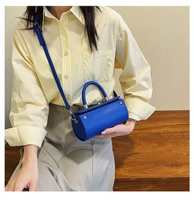Fashionable bright blue cylindrical handbag shown with shoulder strap on a model outfit