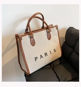 Detalle del bolso tote de lona blanco roto con asas de cuero marrón y bordado de PARIS