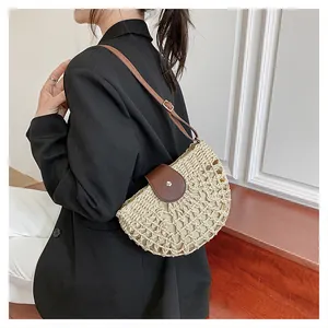 Détail du sac en paille demi-lune avec rabat en cuir marron et ornement argenté