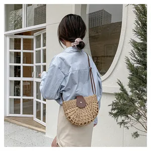 Détail d'un sac à bandoulière en paille tissée avec rabat en cuir brun et bouton pression