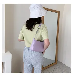 Primer plano de un bolso baguette lila con cadena de plata usado por una modelo