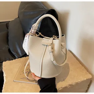 Close-up of cream textured leather bucket bag with brand logo and silk scarf handle