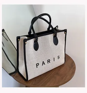 Detalle del bolso tote de lona beige con ribete de cuero negro y estampado Paris en madera