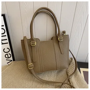Detailed view of brown litchi grain leather handbag with gold metal hardware on knitwear