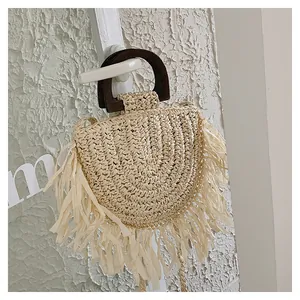 Détail de sac en paille beige avec longues franges et poignée en bois sur mur blanc