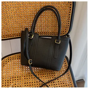Detail shot of black lychee grain leather handbag with gold buckles on a rattan chair