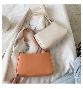 Detalle de bolsos baguette modernos en beige y naranja con correa de cadena sobre tela