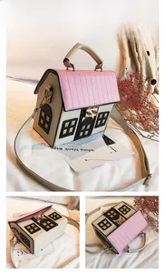 Detail of beige house-shaped crossbody bag featuring pink roof flap and metal lock