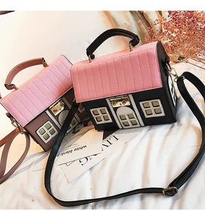 Close-up of house-shaped crossbody bags in pink and black on white bedding with flowers
