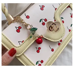 Close-up of cream yellow PU leather crossbody bag with red cherry print and floral gold buckle