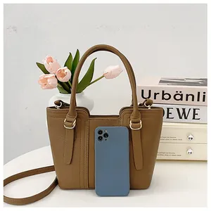Detail of small khaki tote bag with litchi grain texture and gold hardware next to a phone