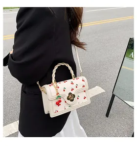 Detail of white crossbody bag featuring cherry print, flower clasp, and woven rope handle