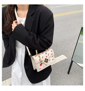 Detail of cream crossbody bag with red cherry print and golden flower twist lock clasp