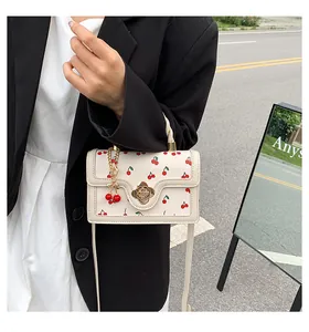 Chic cream crossbody bag featuring red cherry prints and golden floral clasp on a street