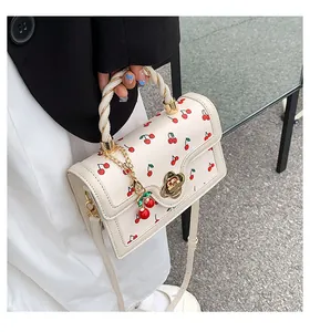Close-up of white crossbody bag with cherry print, flower lock, and woven handle details