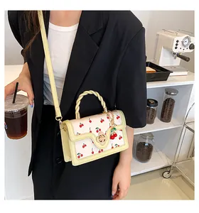 Detail of cream crossbody bag with cherry prints, woven handle and gold twist lock