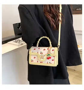 Detail of cream crossbody bag with cherry prints, floral gold lock and woven handle