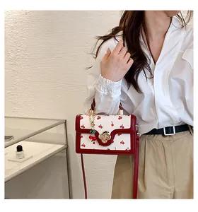 Detail of crossbody bag with cherry print, floral gold lock, and cherry pendant charm