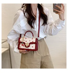 Detail of red cherry print bag with gold flower clasp and twin cherry charm on white leather